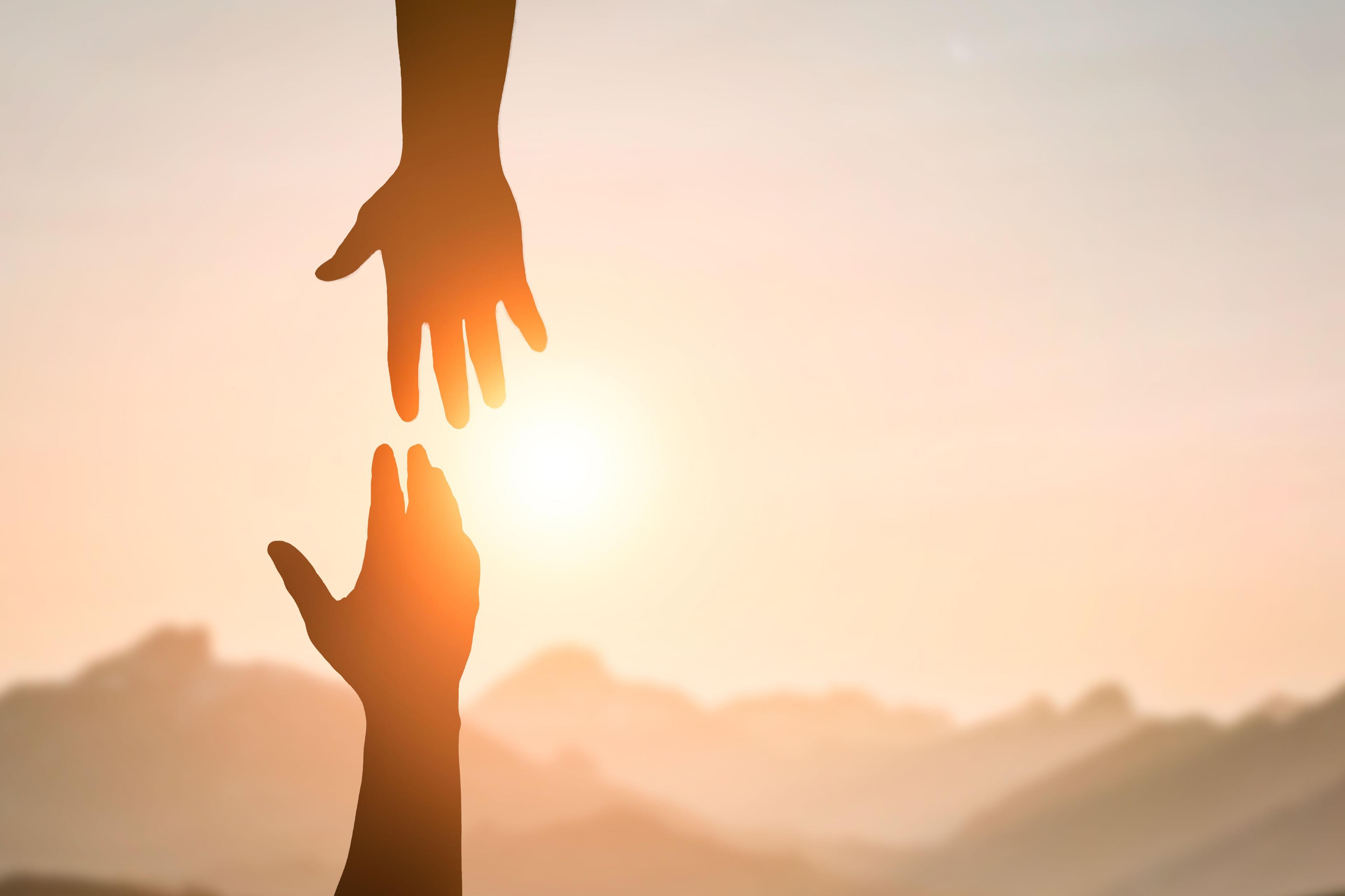 hand reaching out to another hand, sunset in the background