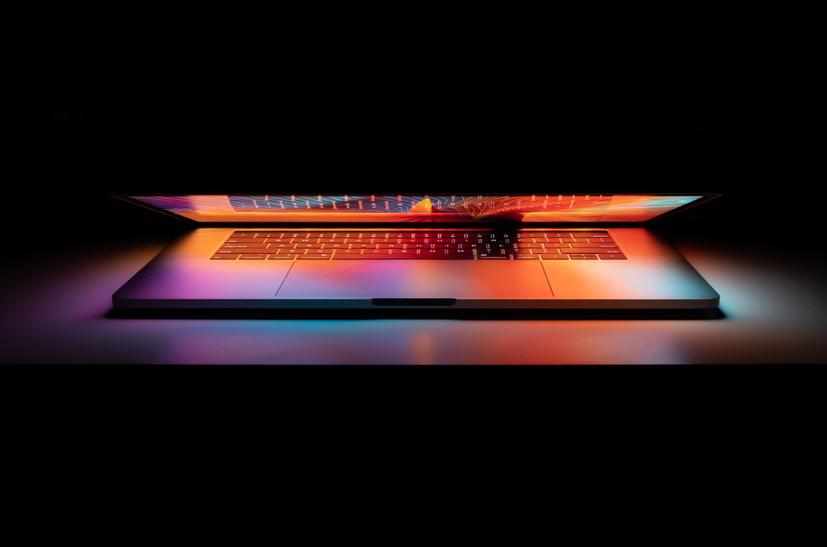 A laptop half closed with multi coloured glow from the screen