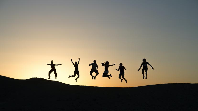 People jumping on a hillside with the sun in the background