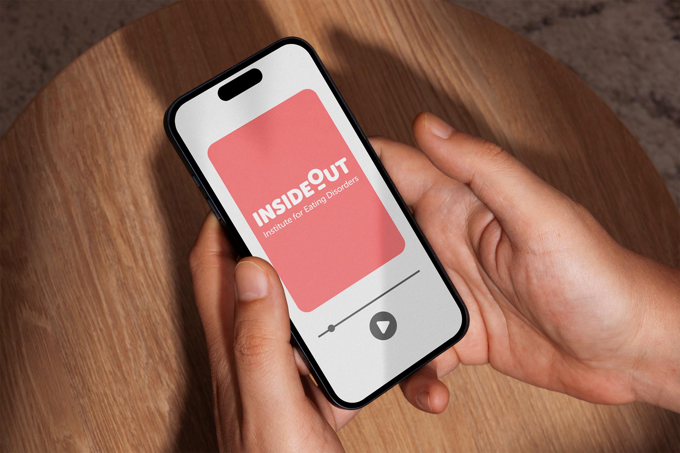 Hands hold a smartphone displaying the "INSIDE OUT Institute for Eating Disorders" logo against a textured wooden surface.
