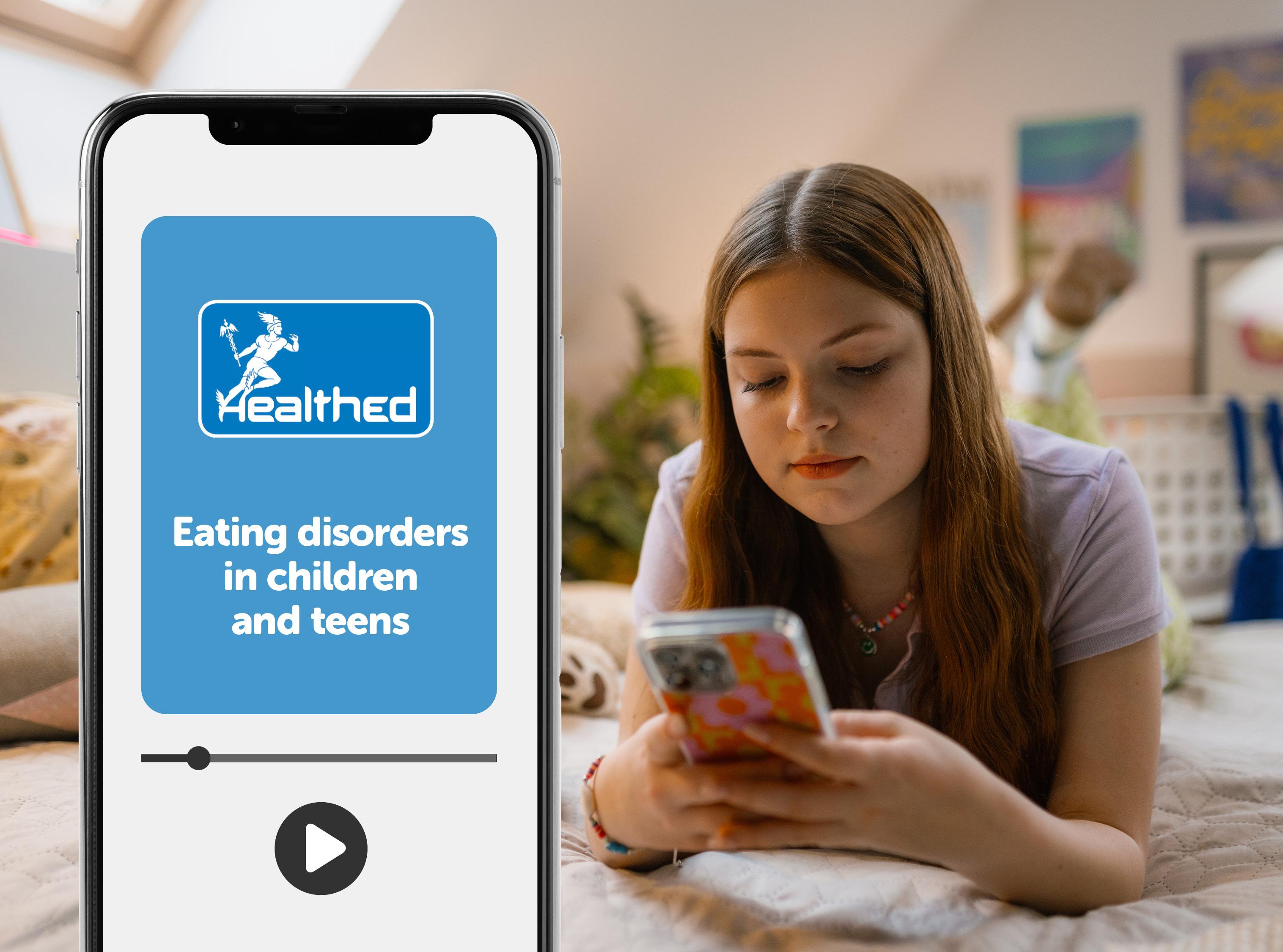 Smartphone displaying a Healthed educational video titled “Eating disorders in children and teens.” A video progress bar and play button appear on the phone screen. In the background, a young person lies on a bed using a mobile phone in a bedroom with soft furnishings and wall art visible.